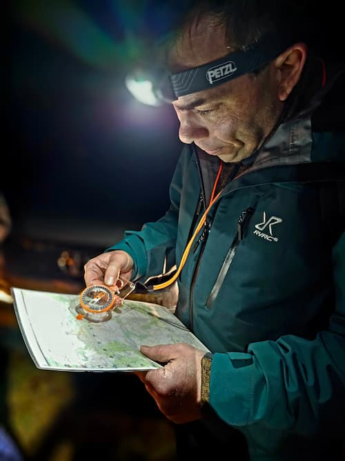 Persoon met een hoofdlamp bepaald met een kompas de route op een kaart