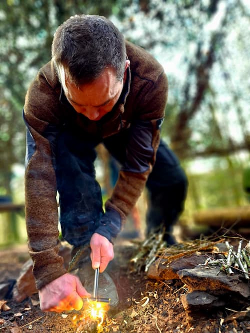 Een man maakt vuur met vuursteen en staal tijdens een bushcrafttraining.