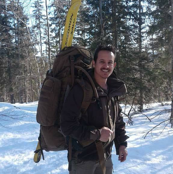Eigenaar en instructeur Dave met een grote rugzak met bomen en sneeuw op de achtergrond.