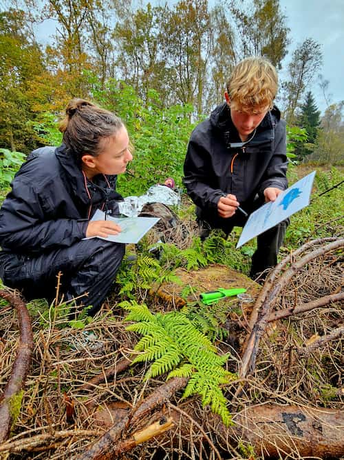 Twee deelnemers bestuderen een kaart en kompas op een open plek in het bos.