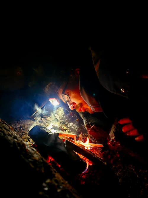 Iemand blaast voorzichtig op het hout om een vuur aan te wakkeren tijdens een nachtoefening.