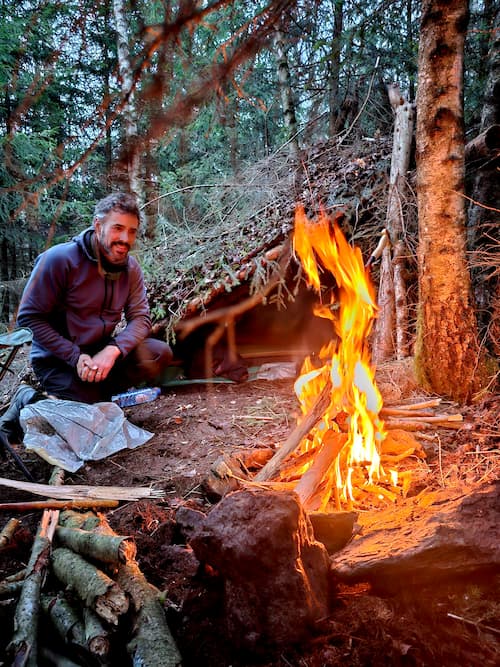 Persoon zittend naast een vuur voor het gebouwde onderkomen